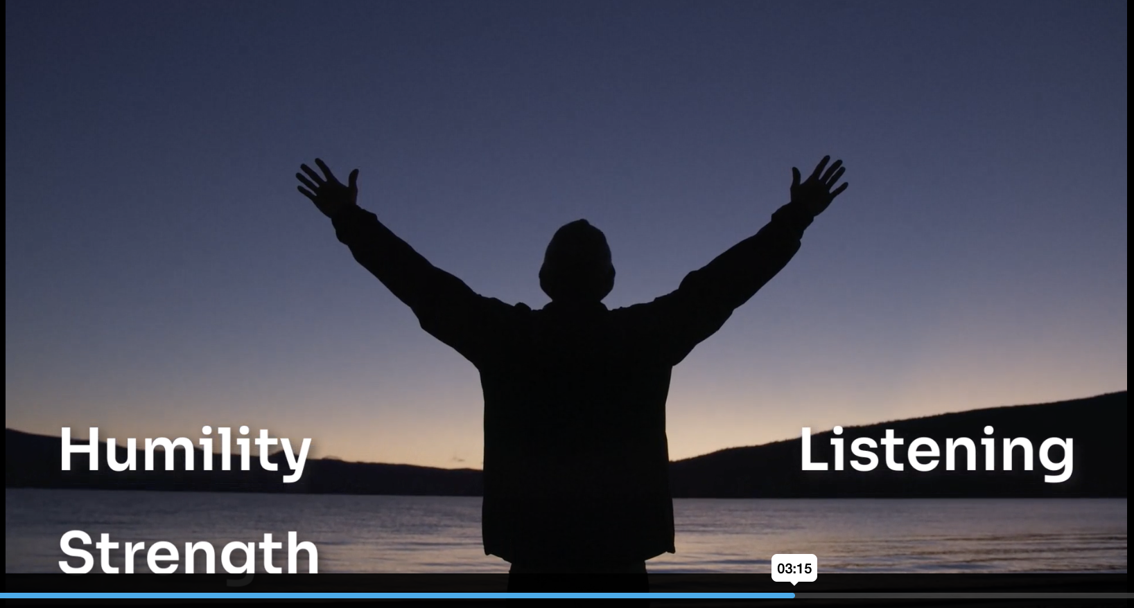 Still from one of the companion videos — a man in silhouette against a dusk sky, arms raised at the edge of a lake, with the words Humility, Strength, and Listening overlaid.